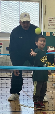 young boy throws a tennis ball with a coach